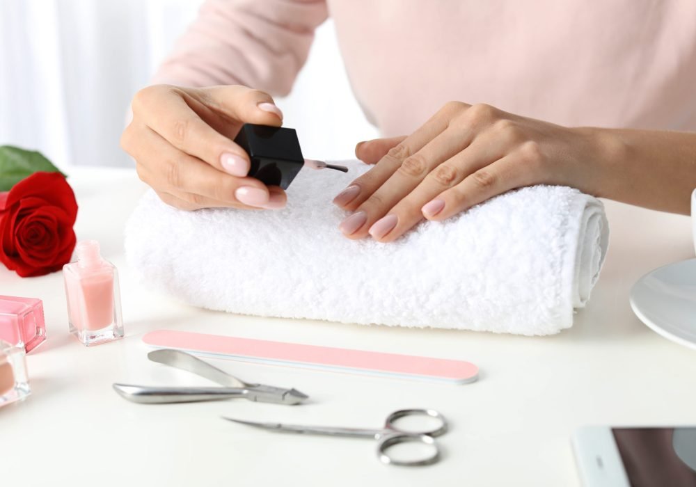 Woman applying nail polish at table, closeup. At-home manicure