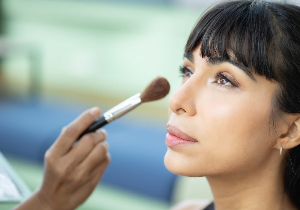Make-up artist work on woman business model.Artist applying powder with a brush on model's cheeks, selective focus on model .