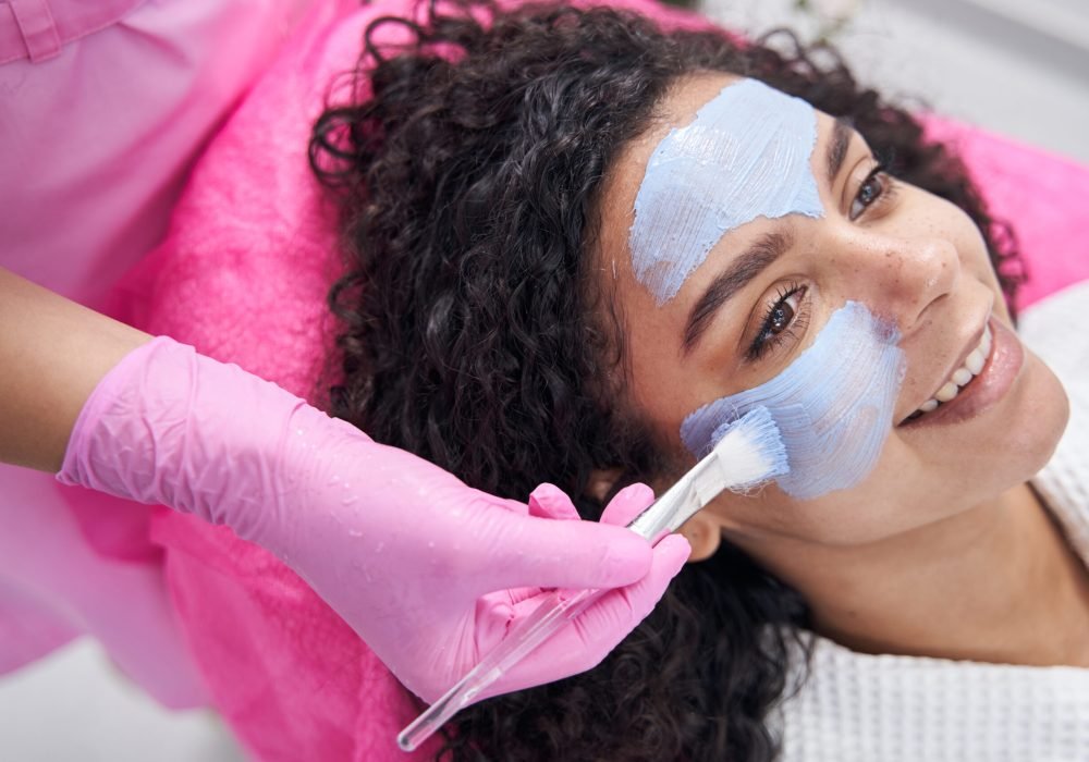 Satisfied lady lies on her back while a beauty product is applied to her face with a brush